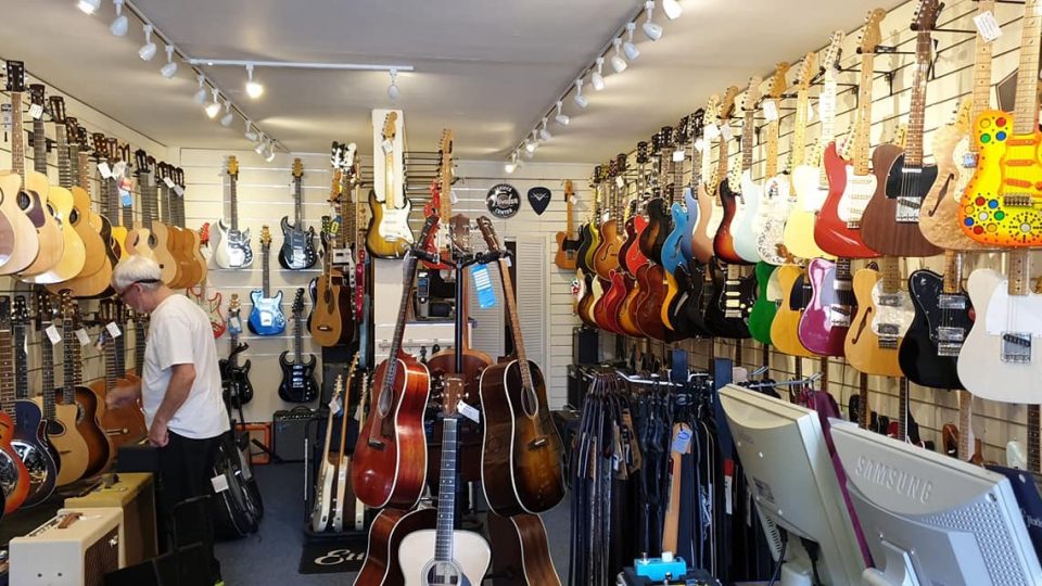 An elderly white, masculine adult looking at some acoustic and electric guitars.