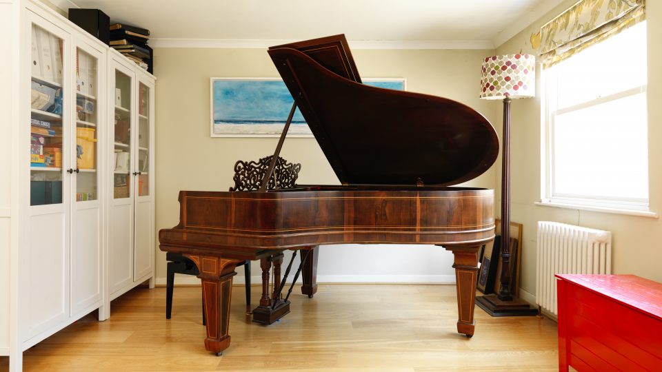 A grand piano in a room with a white bookcase and a red chest