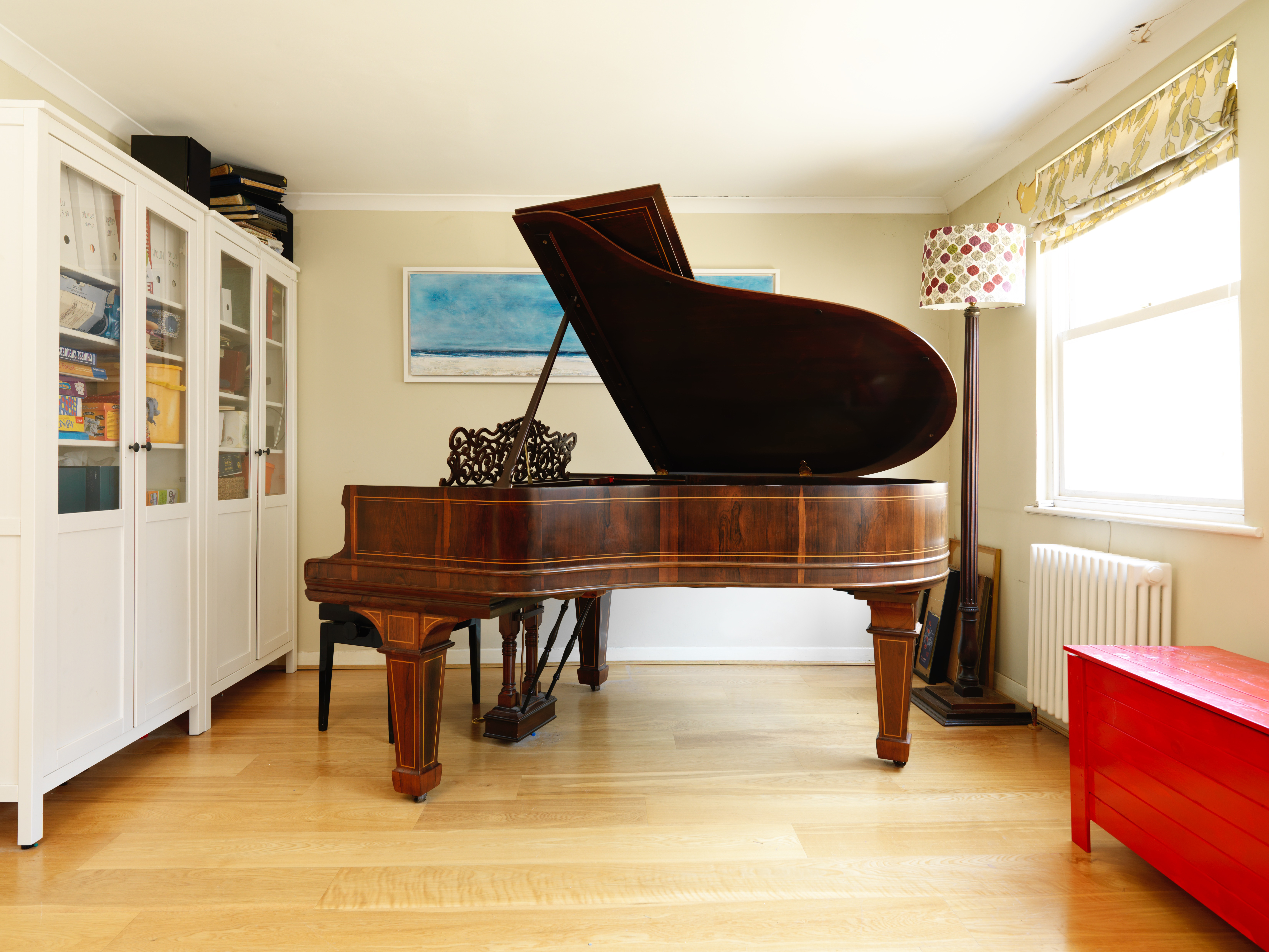 A grand piano in a room with a white bookcase and a red chest