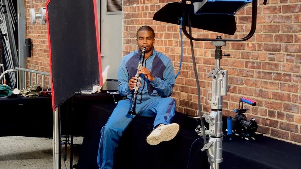 A black, masculine adult playing the clarinet behind the scenes