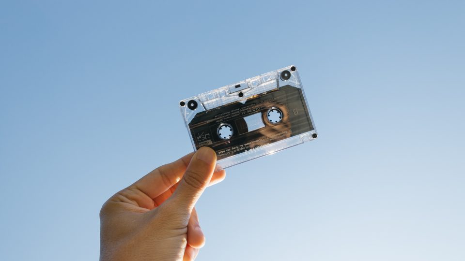 A white person holding a cassette tape with a blue sky background