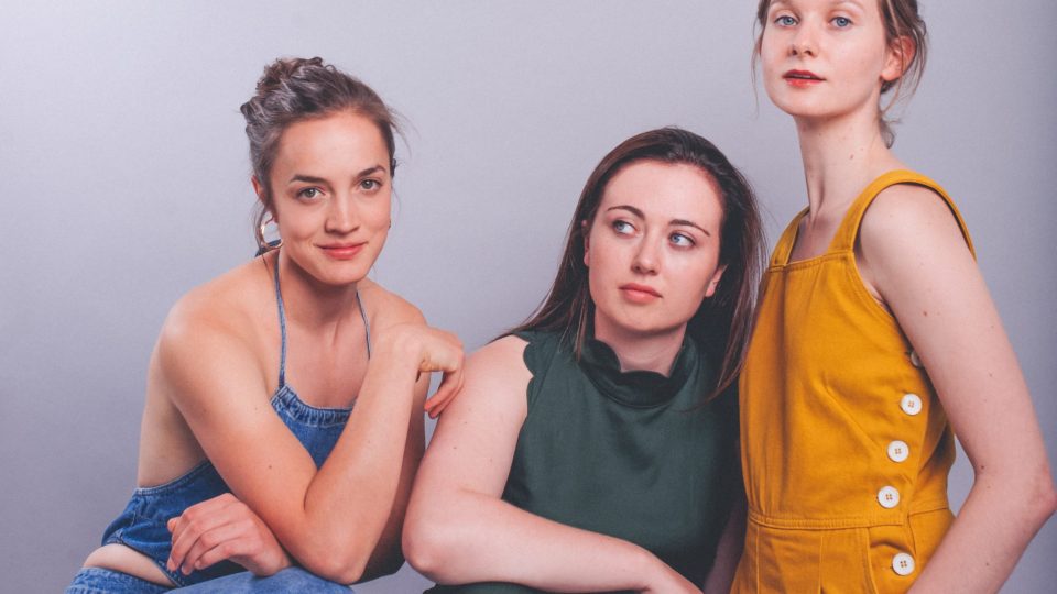 3 white, feminine people are posing and standing in front of a white background