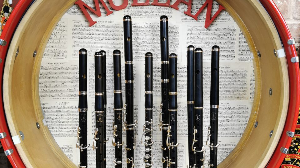 Some clarinets on a wooden stand inside a circular case with some sheet music in the background,