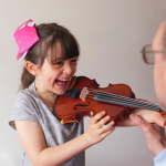 Smiling girl holding violin while her teacher helps position her hands