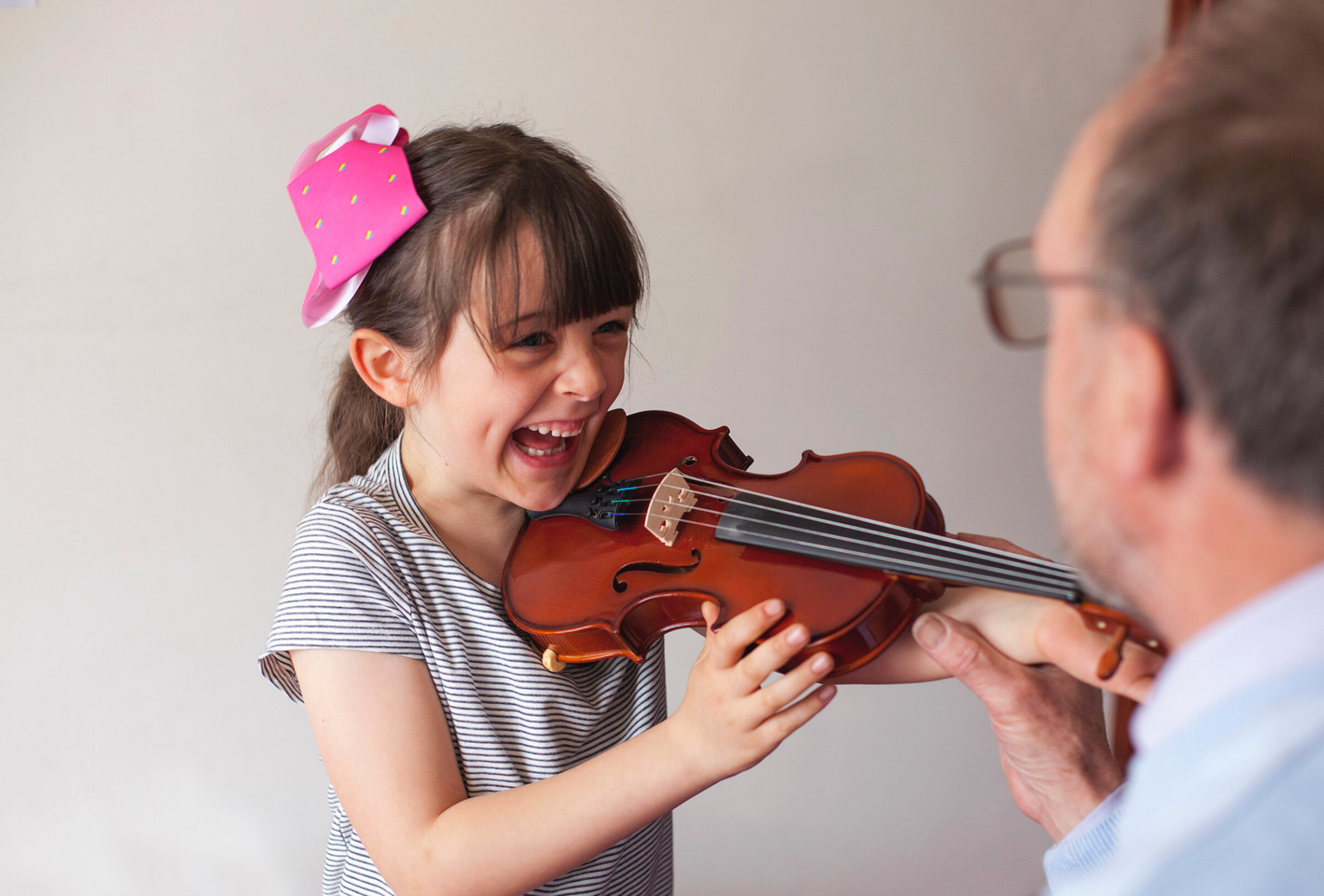 Smiling girl holding violin while her teacher helps position her hands