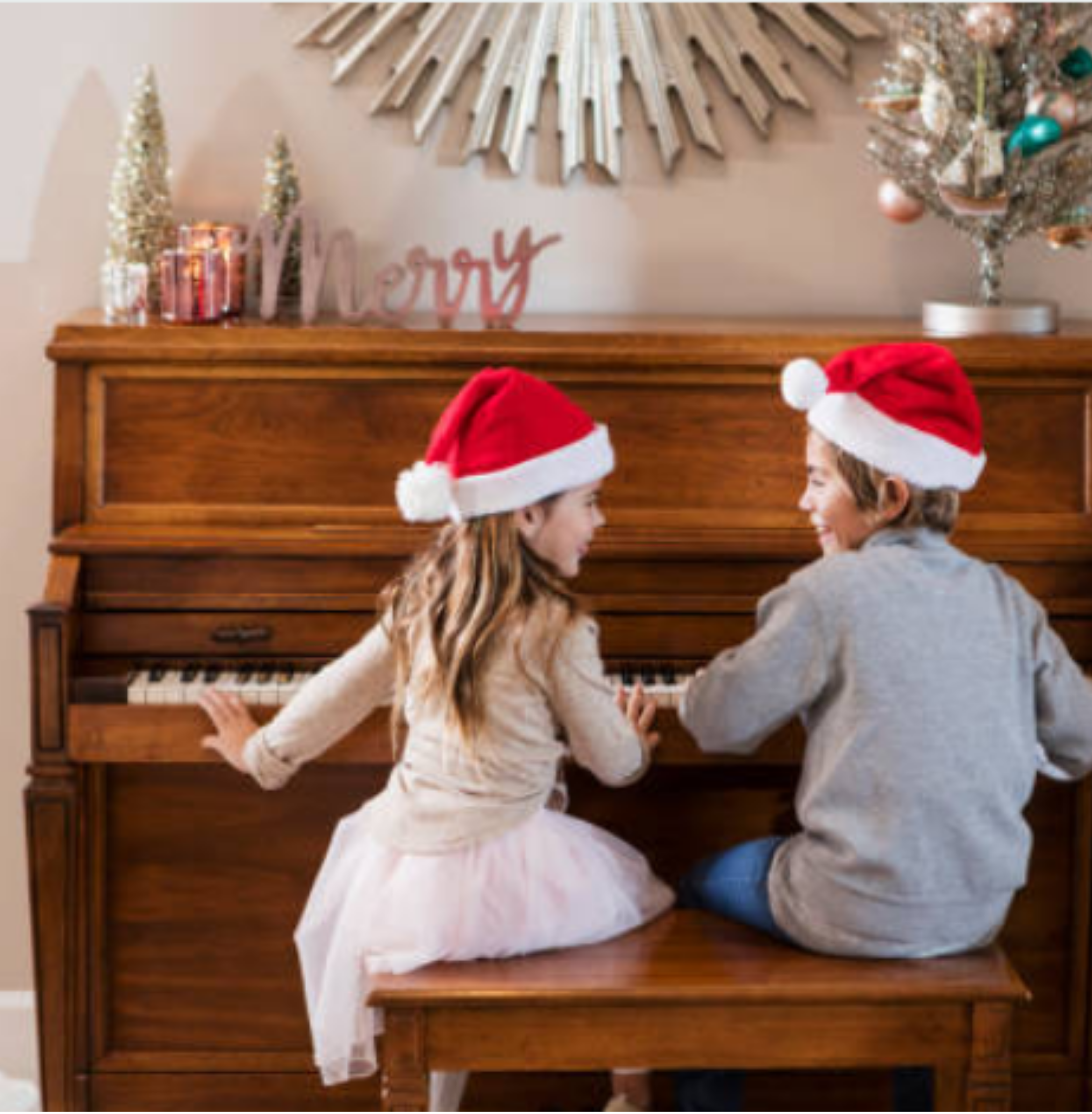 two children wearing Christmas hats playing the piano