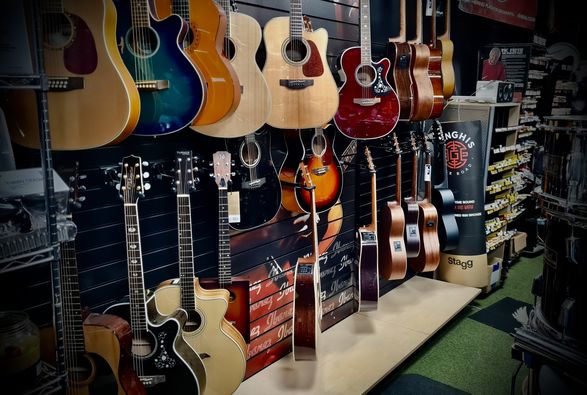 A wall display of a dozen acoustic guitars of various shades, colours and shapes