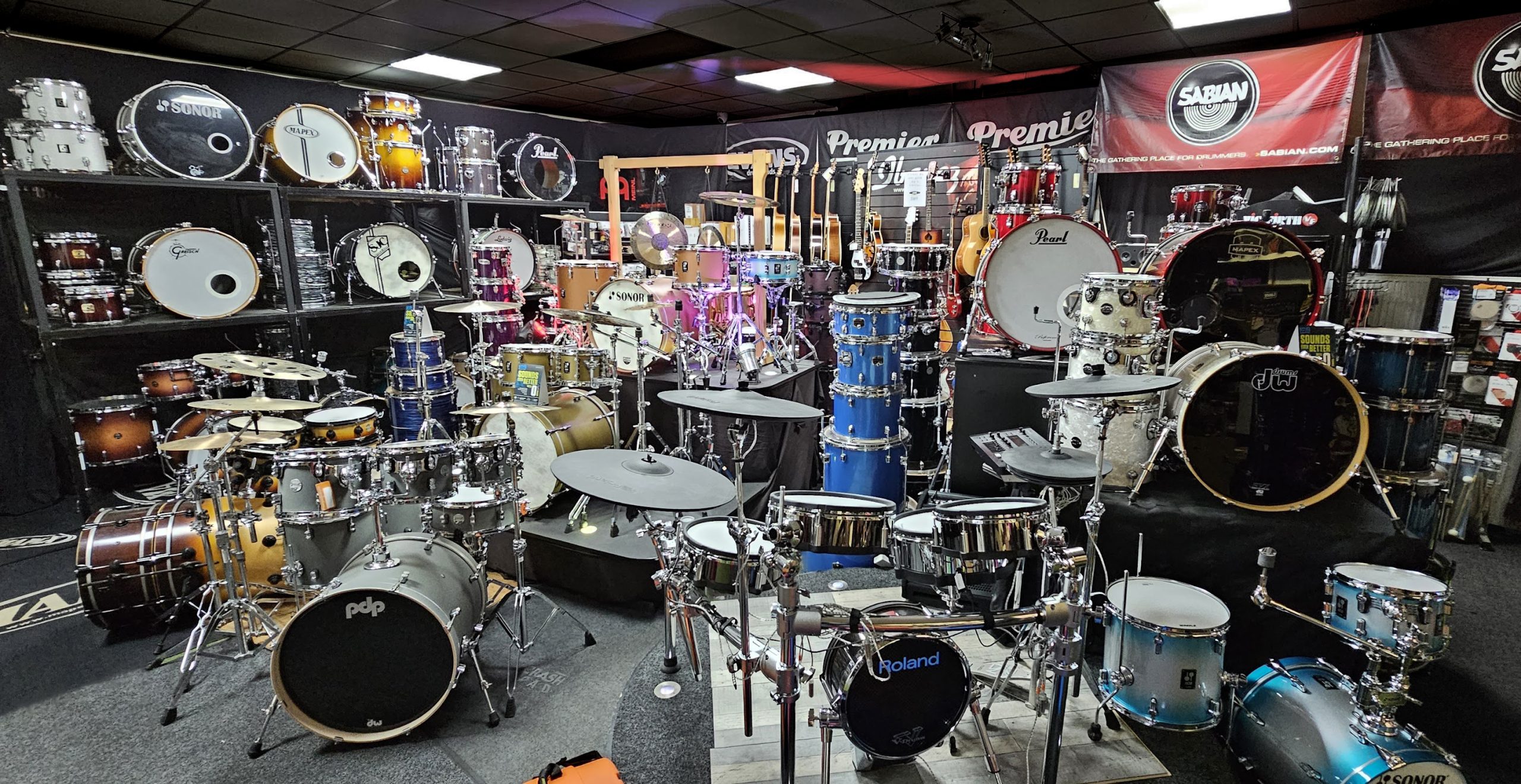 A corner of the Rockem shop with dozens of drums and drum kits, with a wall of guitars at the back
